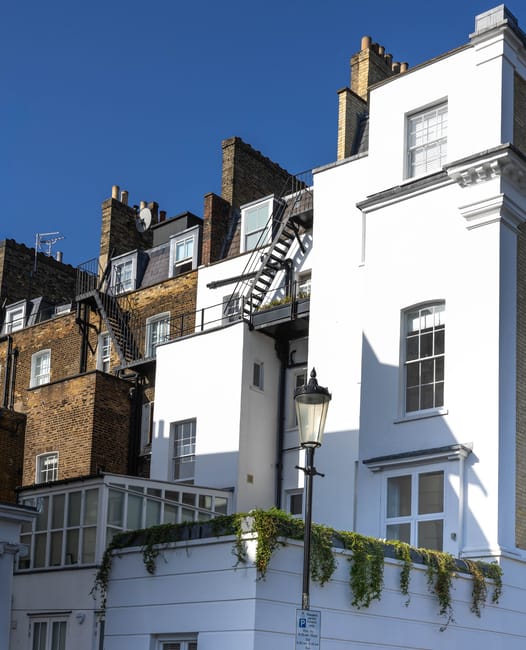A narrow pedestrian alleyway in Belgravia, surrounded by residential buildings with brick and white-painted facades. On the left side, there is a wooden planter box with greenery and two decorative ou