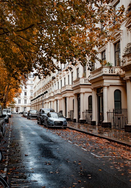 The image depicts a residential street with a row of elegant, white-painted Victorian-style terraced houses featuring decorative columns, black wrought-iron railings, and large windows. The pavement i